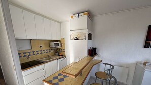 A compact kitchen with white cabinets, a microwave, a sink, and a small refrigerator. There are two bar stools and a tiled backsplash with a geometric pattern. - Air-Conditioned 3-Room Apartment with Terrace, Close to Beach (Port-la-Nouvelle)