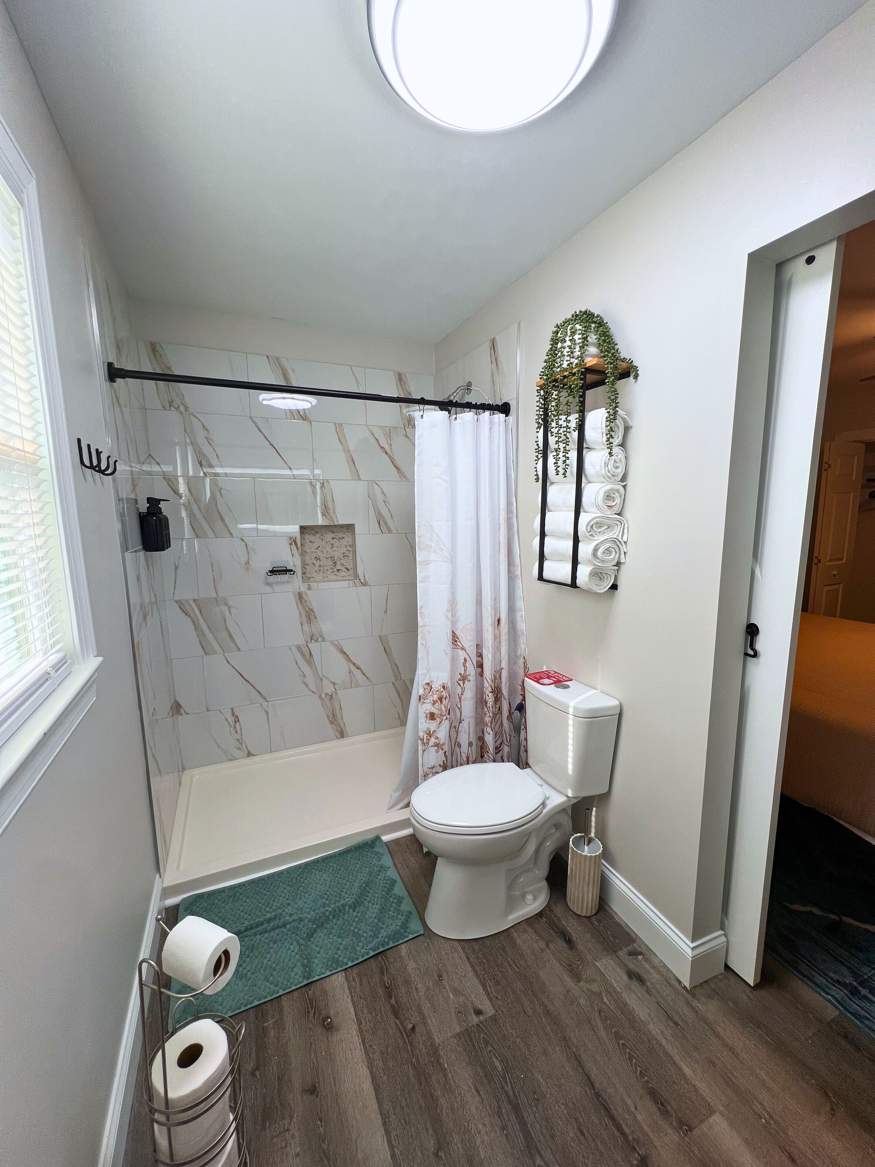 A bathroom with a shower, toilet, and a small rug.