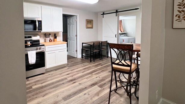 Een ruime keuken met witte kastjes, een magnetron en een eethoek met een houten tafel en stoelen.
