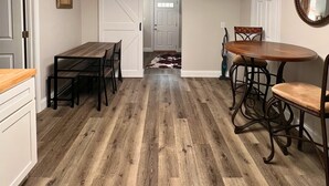 Een kamer met een houten vloer, een eettafel met stoelen, een keuken met een aanrecht en een deur naar een andere kamer.