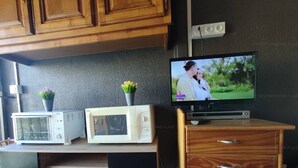 Ett kök med träskåp, en mikrovågsugn, en tv och ett litet skåp med en låda.