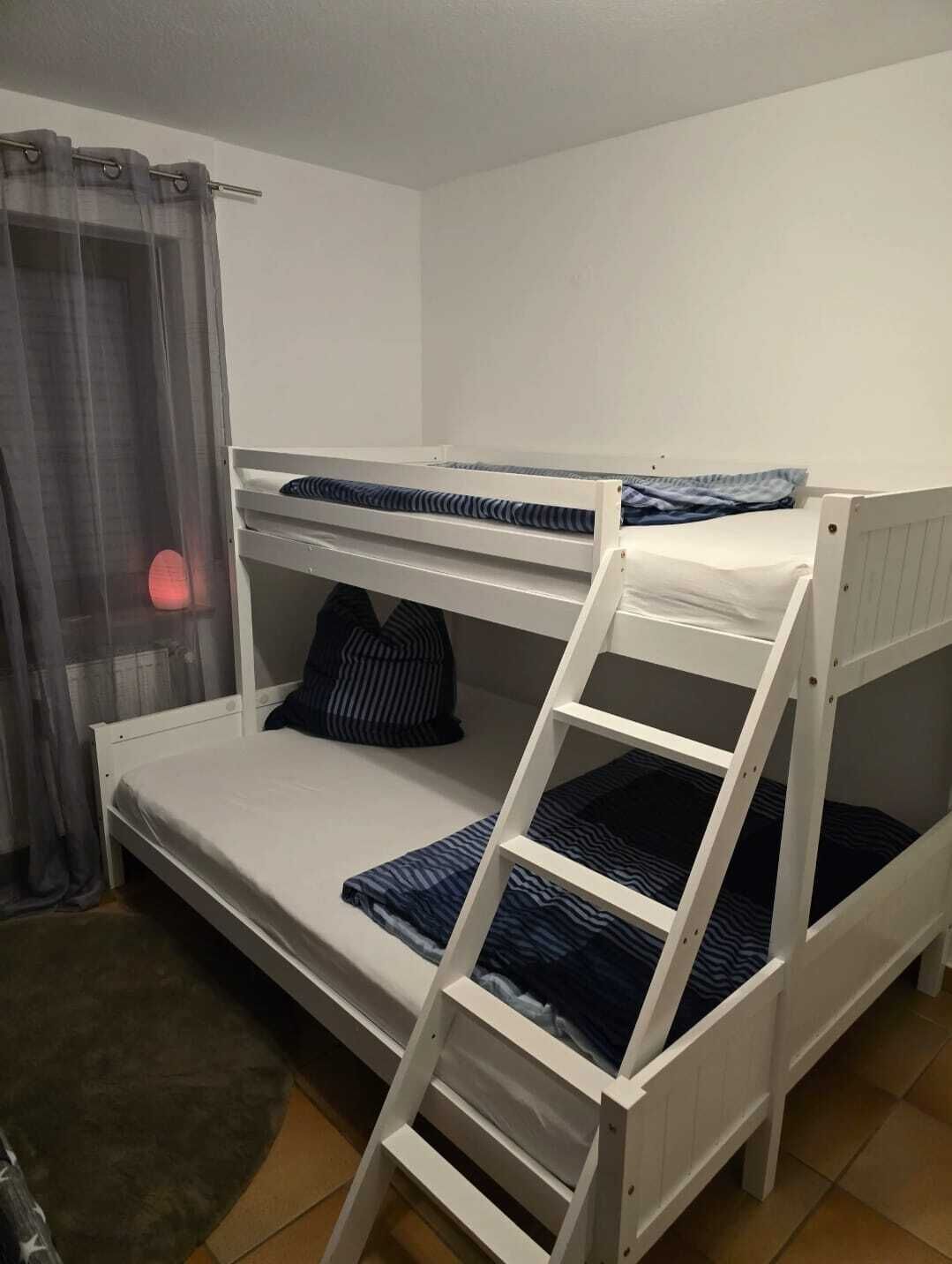 A bunk bed room with a ladder, a small window with curtains, and a red light on the wall.