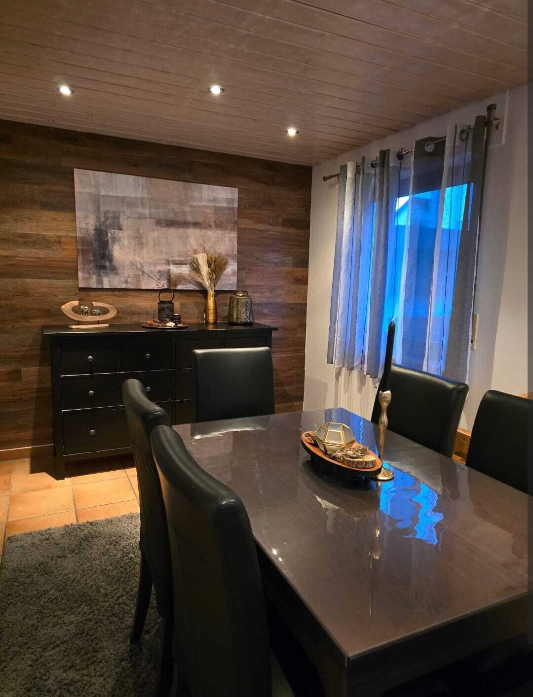 Ein moderner Essbereich mit einem dunklen Holztisch, schwarzen Stühlen und einem schwarzen Schrank mit Dekoration.