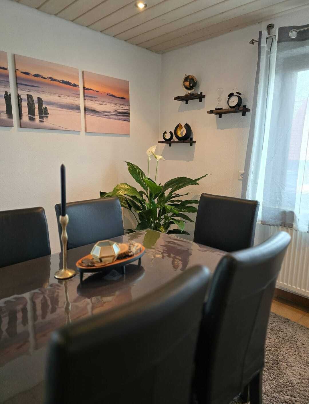 Ein Essbereich mit einem Glastisch, schwarzen Stühlen, einer Topfpflanze und Kunstwerken an der Wand.