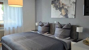 Un dormitorio moderno con una cama grande, paredes grises, una lámpara de techo y una obra de arte abstracta.