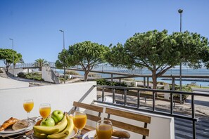 Un coin repas avec une table mise pour le petit-déjeuner, offrant une vue sur la côte, avec des arbres et un pont.