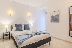 Une chambre à coucher comprenant un lit, deux tables de chevet, deux lampes fixées au mur, une œuvre d’art encadrée et un miroir.