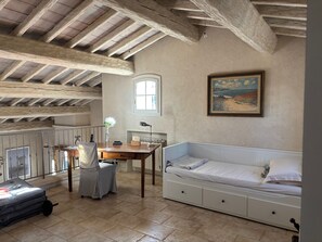 Ein Zimmer mit freiliegenden Holzbalken, einem Schreibtisch mit Lampe, einem Bett und einem Gemälde an der Wand.