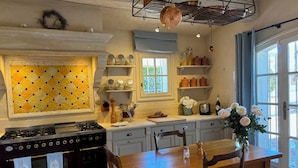 A kitchen with a gas stove, oven, wooden table, chairs, and a window with curtains. - Luxurious Ocean View Home in South of France, Close St. Tropez (Fréjus)