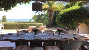 An outdoor dining area with wicker furniture, a table set for a meal, and a view of the sea. - Luxurious Ocean View Home in South of France, Close St. Tropez (Fréjus)