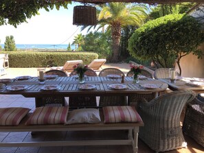 Ein Essbereich im Freien mit Korbmöbeln, einem für eine Mahlzeit gedeckten Tisch und Blick auf das Meer.