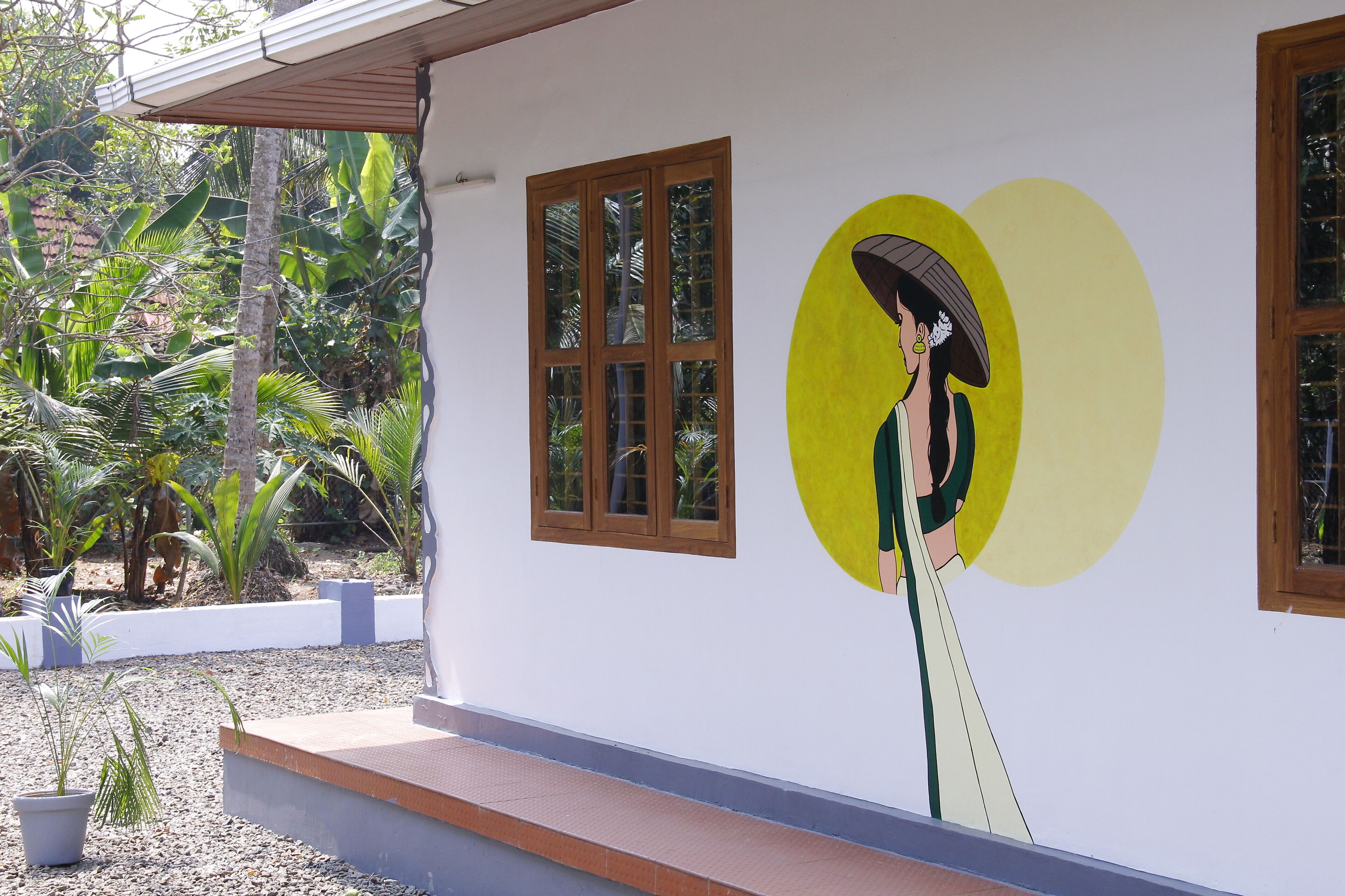 A building with a mural of a woman holding a parasol, a window, and a small garden area with potted plants.