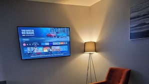 Een moderne woonkamer met een flatscreen televisie aan de muur, een staande lamp, een rode fauteuil en een salontafel.
