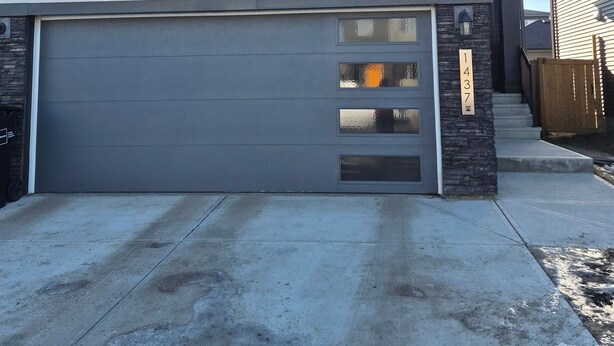 Een tweelaags huis met garage, een accentmuur van natuursteen en een houten omheining.