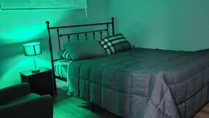 Een slaapkamer met een bed, een stoel, een nachtkastje en een lamp.