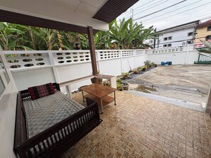 A covered outdoor seating area with a wooden bench and table, surrounded by potted plants and a white fence. - 3BR Family Villa - 1 km to Chalong Pier With Wifi (Chalong)