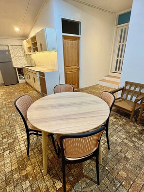 A dining area with a round table and four chairs, a kitchen with white cabinets and a wooden door, and a wooden bench outside. - 3BR Family Villa - 1 km to Chalong Pier With Wifi (Chalong)