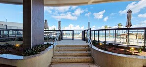 Un conjunto de escalones exteriores conduce a una terraza con vistas despejadas al océano, rodeada por una barandilla metálica y equipada con sombrillas.