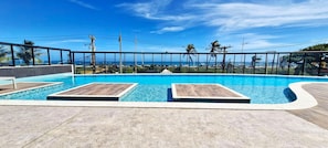 Una piscina con lettini in legno, circondata da un solarium piastrellato e una ringhiera in metallo.