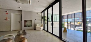 Um lobby moderno com porta de vidro que dá para o exterior, um balcão de recepção, um sofá branco e uma mesa pequena com objetos decorativos.