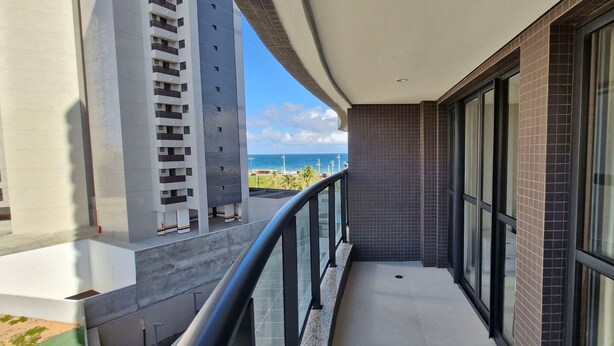 A balcony with a view of the ocean and a building with a modern design. - COJAG0102 - Beach Class Jaguaribe (Salvador)