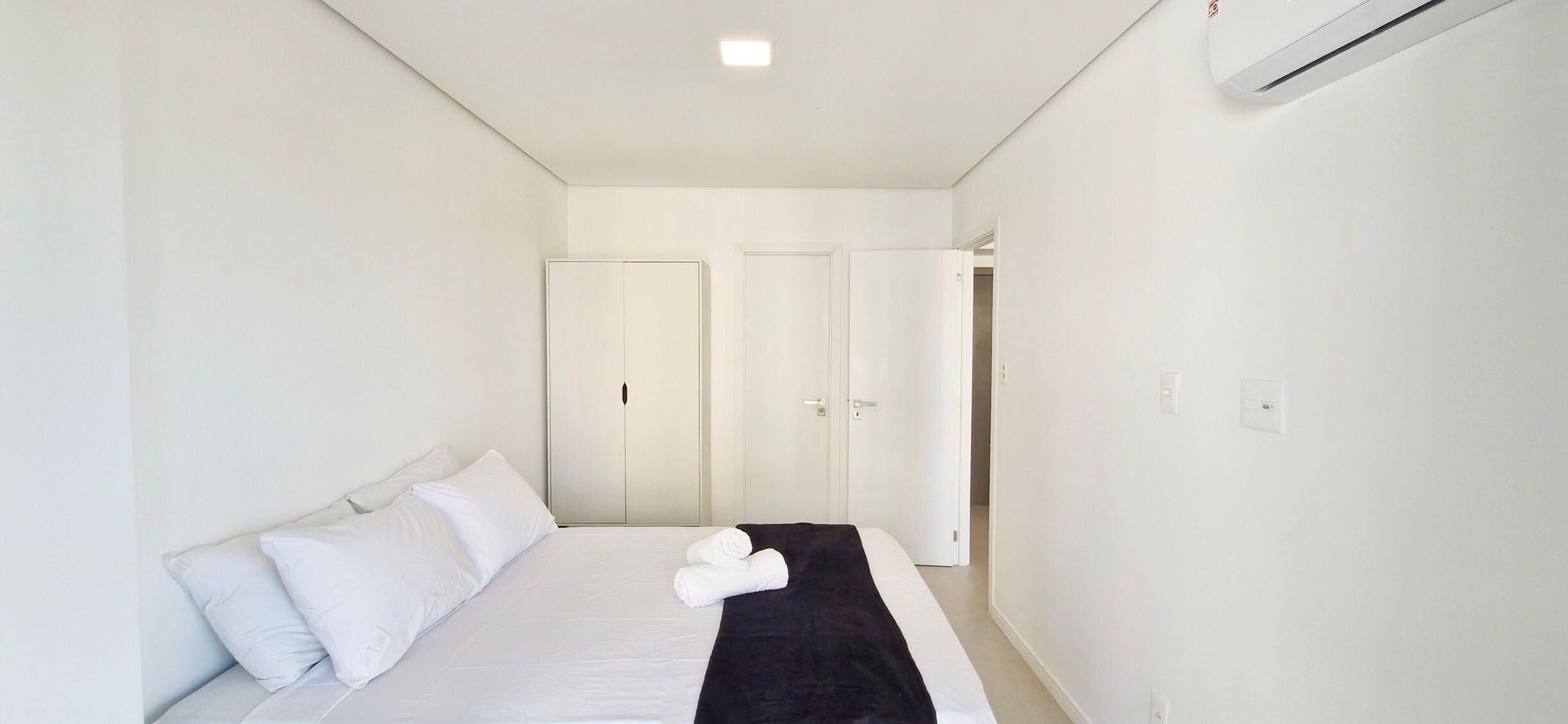 Habitación de hotel minimalista con cama, paredes blancas y puerta que da a otra habitación.