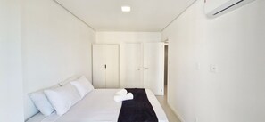 Una camera d'albergo dal design minimalista, con un letto, pareti bianche e una porta che conduce a un'altra stanza.