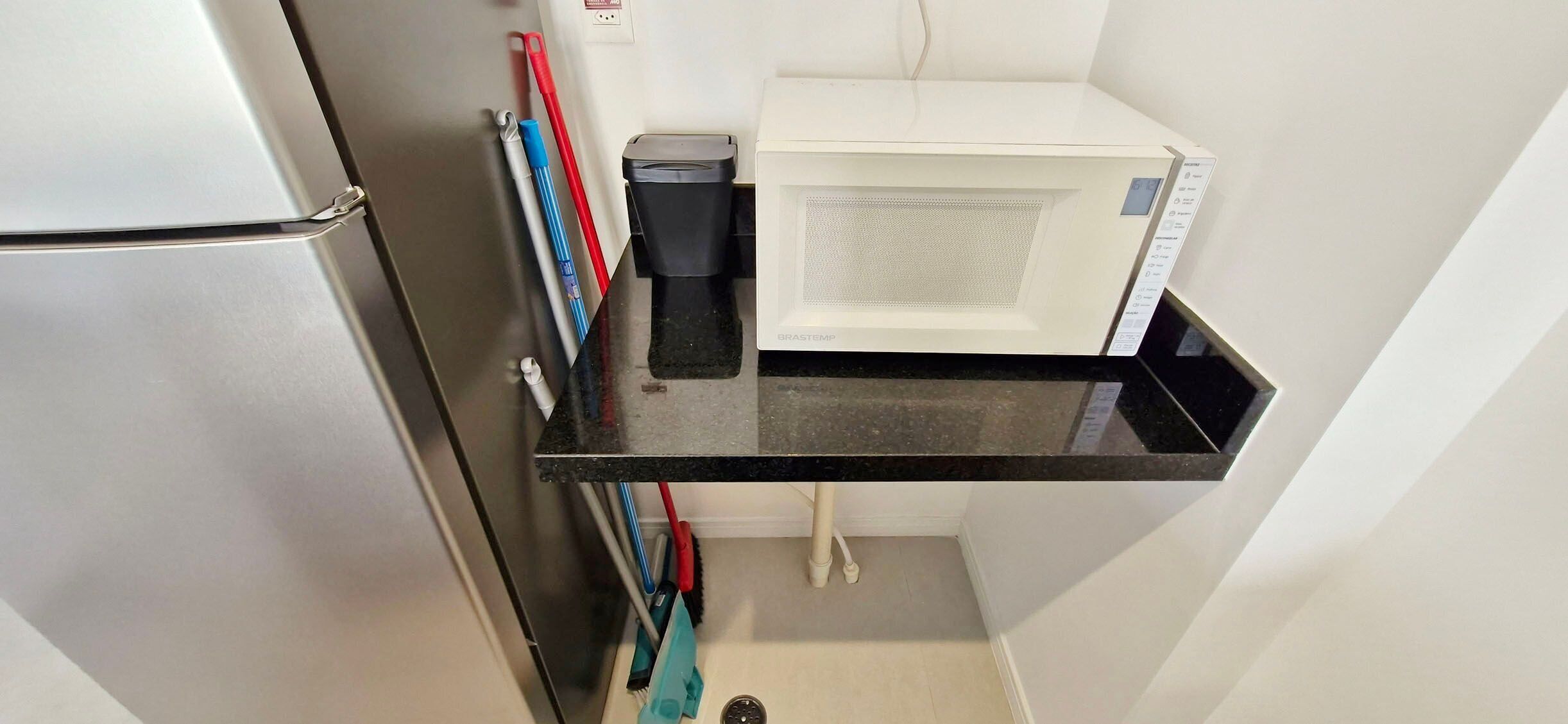 Cocina compacta con refrigerador, microondas y encimera negra.