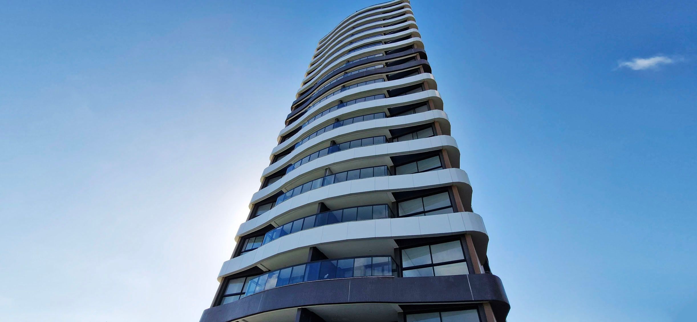 Um edifício alto e moderno, com várias varandas e janelas grandes.