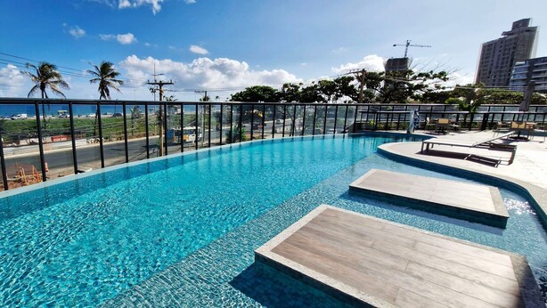 Una piscina con agua azul cristalina, rodeada por una barrera de vidrio y con vistas a una playa y al horizonte urbano.