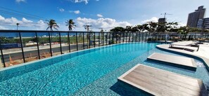 Una piscina con agua azul cristalina, rodeada por una barrera de vidrio y con vistas a una playa y al horizonte urbano.