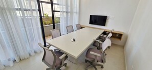 Una sala conferenze con un grande tavolo, sei sedie, una televisione a parete e una finestra con tende leggere.