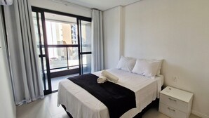 Una habitación de hotel con cama, mesita de noche y ventana con cortinas.