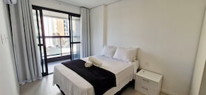 Una habitación de hotel con cama, mesita de noche y ventana con cortinas.