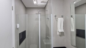 Un baño moderno con ducha de vidrio, una toalla blanca colgada en un perchero y un espejo grande.