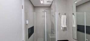 Un baño moderno con ducha de vidrio, una toalla blanca colgada en un perchero y un espejo grande.