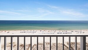 Blick auf einen Strand vom Balkon mit Geländer, klarer Himmel und ruhige See.