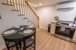 A dining area with a round table set for four, a staircase, and a kitchen with an oven and a trash can. - Roanoke Roost | Secluded | 2BR | Fire pit | Cozy (Roanoke)