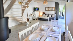 A dining area with a table set for four, a sofa, a television, and a staircase. - Large Holiday Homes With Fireplace and Garden (Postomino)