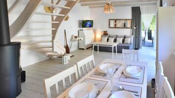 A dining area with a table set for four, a sofa, a television, and a staircase.