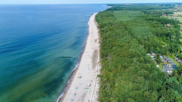 An aerial view of a beach with a dense forest on one side and a row of cabins on the other. - Large Holiday Homes With Fireplace and Garden (Postomino)