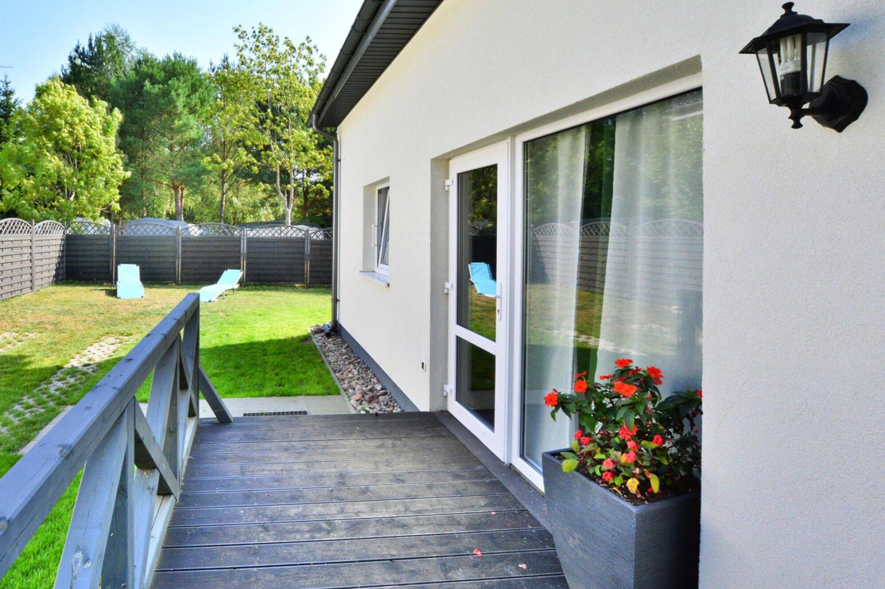 A wooden deck leading to a house with a sliding glass door, a small window, and a wall-mounted outdoor light fixture.