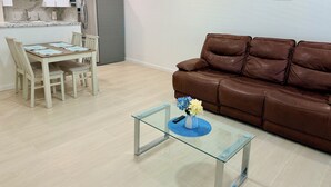 Un salon moderne avec un canapé en cuir marron, une table basse en verre ornée d’un vase de fleurs et un coin repas avec une table et des chaises en bois.