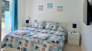 Une chambre à coucher avec un lit, des tables de chevet, un ventilateur de plafond et des œuvres d’art accrochées au mur.