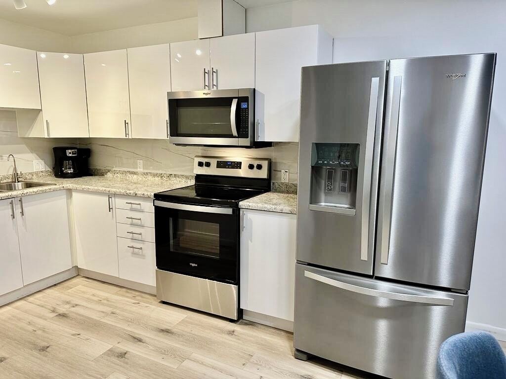 Una cocina moderna con gabinetes blancos, un refrigerador de acero inoxidable, un microondas integrado y un horno.