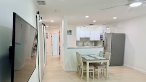 Une cuisine moderne avec des meubles blancs, un four encastré et un réfrigérateur. On y trouve également un coin repas avec une table et des chaises en bois.