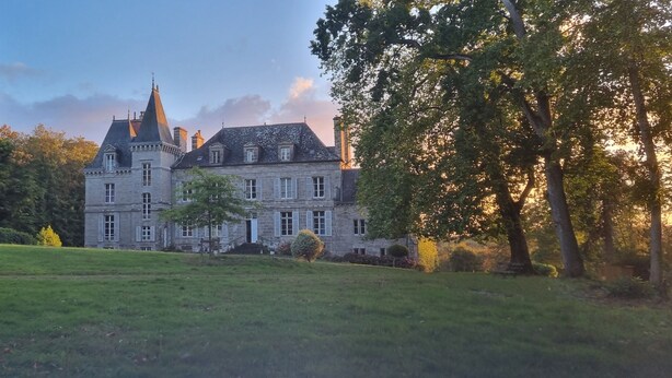 A large, historic stone building with multiple chimneys and a prominent tower, surrounded by lush greenery and a well-maintained lawn. - Private 2-bedroom apartment at Château de La Coste (Saint-Julien)