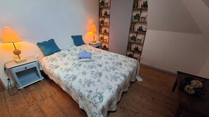 A bedroom with a floral bedspread, two bedside lamps, a nightstand, a bookshelf, and a wooden floor. - Private 2-bedroom apartment at Château de La Coste (Saint-Julien)