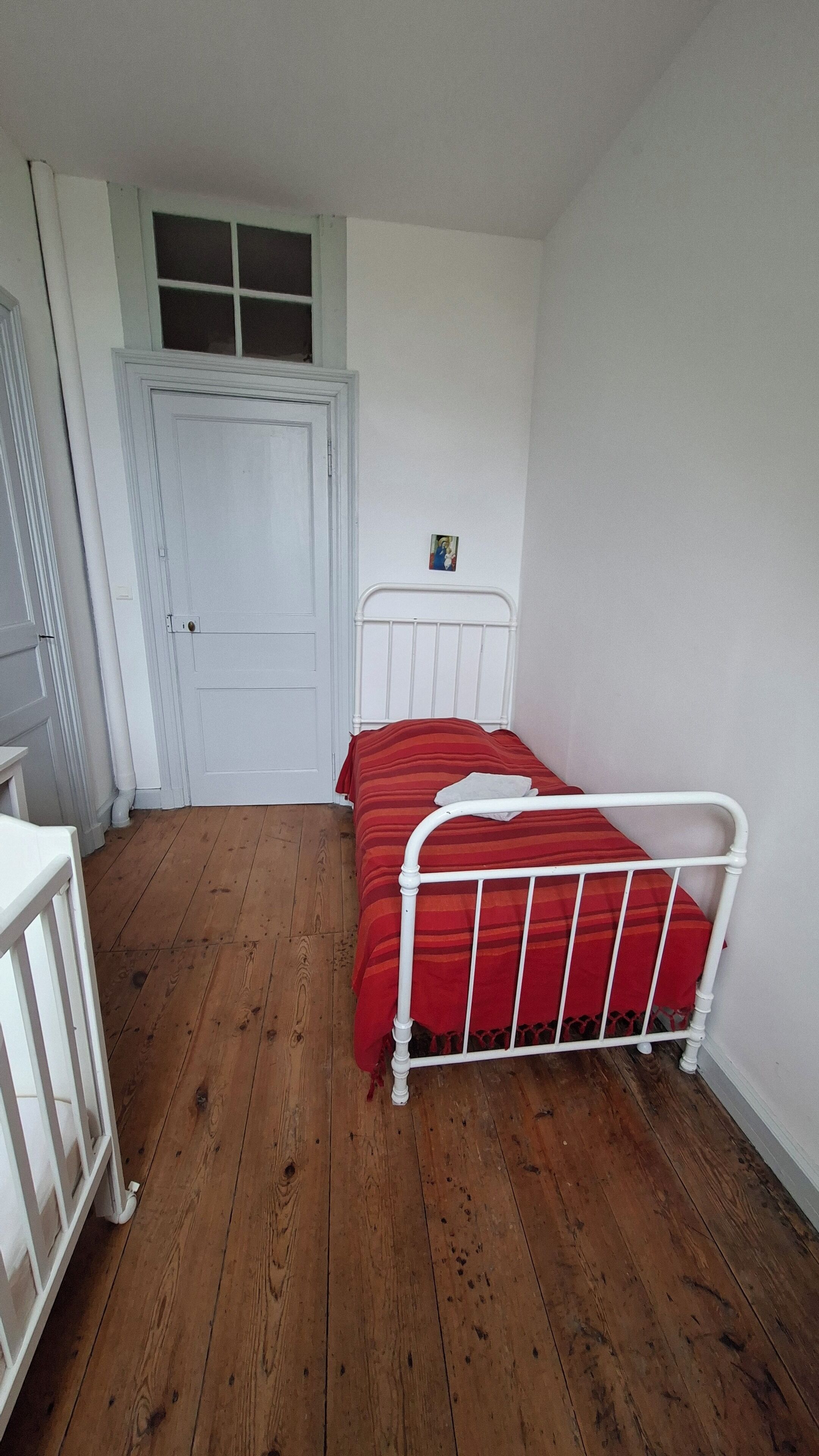 A bedroom with a white metal bed frame, a red striped bedspread, and a white door.