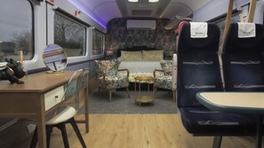 Een treincoupé met een bed, twee stoelen, een tafeltje en een bureau met spiegel en klok.